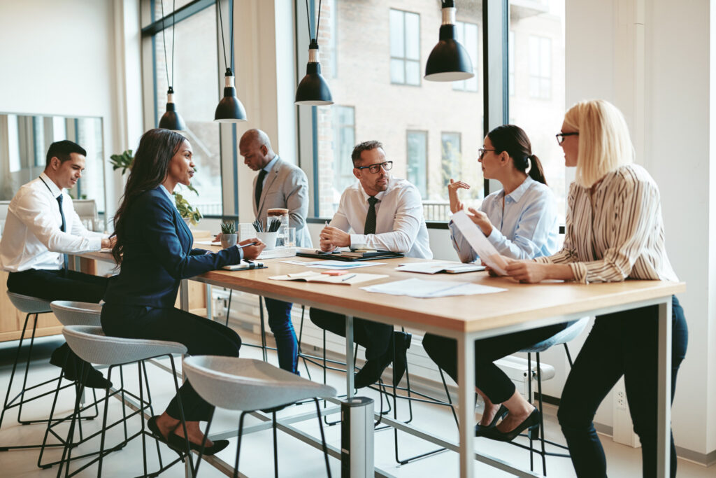 Diverse group of businesspeople talking together around an office table.