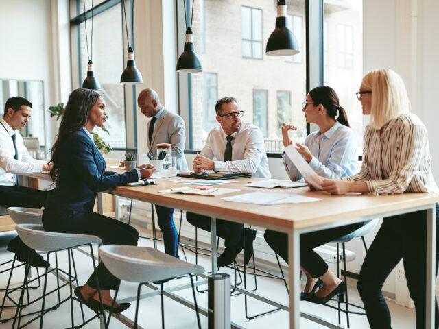 Diverse group of businesspeople talking together around an offic Diverse group of businesspeople talking together around an office table.